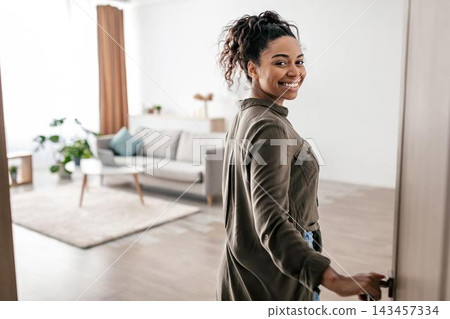 Happy Young Black Woman Smiling While Opening Door In Modern Living Room At Home, Welcoming Atmosphere. Confident Female Engaging With Space, Interior Design, And Lifestyle Concept. Happy Young Black Woman Smiling While Opening Door In Modern Living Room At Home, Welcoming Atmosphere. Confident Female Engaging With Space, Interior Design, And Lifestyle Concept. 143457334