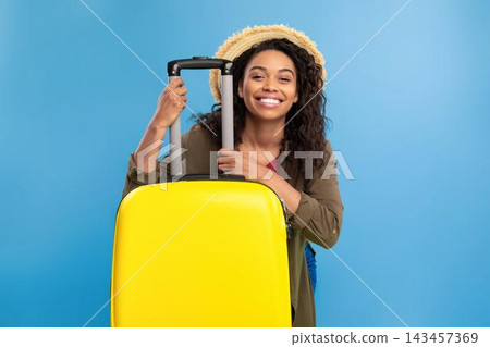 Happy Smiling Black Woman Holding Yellow Luggage, Excitedly Preparing For Trip, Standing Indoors With Blue Background, Ready For Adventure, Travel Concept. 143457369