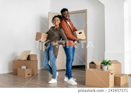 Smiling African American Young Couple Together Holding Moving Boxes In Modern Living Room, Ready For New Home Experience. Joyful Moment Captured In Bright Indoor Setting, Home And Lifestyle Concept. Smiling African American Young Couple Together Holding Moving Boxes In Modern Living Room, Ready For New Home Experience. Joyful Moment Captured In Bright Indoor Setting, Home And Lifestyle Concept. 143457371