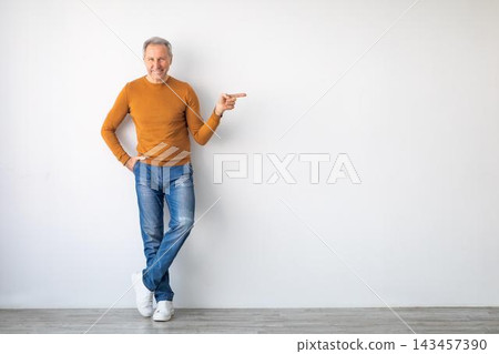 Smiling Middle-aged Caucasian Man In Casual Clothing Pointing Forward While Standing Against A Plain Wall At Home. Portraying Confidence And Readiness To Engage In Business Discussion. Smiling Middle-aged Caucasian Man In Casual Clothing Pointing Forward While Standing Against A Plain Wall At Home. Portraying Confidence And Readiness To Engage In Business Discussion. 143457390