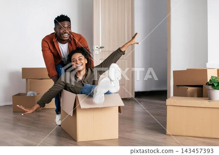 Joyful Black Couple, Young Adults, Smiling And Playing Together In Cardboard Box At New Home, Celebrating Life Transition In Cozy Setting, Enjoying Each Other's Company, Moving Concept. Joyful Black Couple, Young Adults, Smiling And Playing Together In Cardboard Box At New Home, Celebrating Life Transition In Cozy Setting, Enjoying Each Other's Company, Moving Concept. 143457393