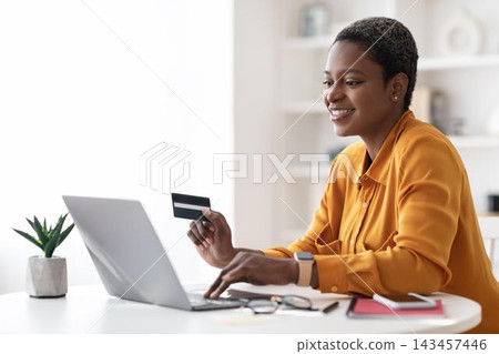 Smiling African American Woman Shopping Online With Credit Card While Using Laptop In Home Office. Focused And Happy Female Engaging In E-commerce Activity At Modern Workspace. Business Concept. Smiling African American Woman Shopping Online With Credit Card While Using Laptop In Home Office. Focused And Happy Female Engaging In E-commerce Activity At Modern Workspace. Business Concept. 143457446