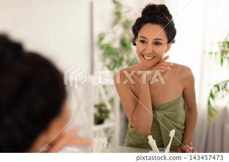 Smiling Young Middle Eastern Woman Applying Skincare Cream In Front Of Mirror At Home, Engaged In Daily Beauty Routine. Taking Care Of Skin With Natural Products In Relaxing Environment. Smiling Young Middle Eastern Woman Applying Skincare Cream In Front Of Mirror At Home, Engaged In Daily Beauty Routine. Taking Care Of Skin With Natural Products In Relaxing Environment. 143457473