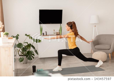 Focused Young Black Woman Engaging In Yoga Pose At Home On Exercise Mat, Enhancing Flexibility And Strength In A Bright And Comfortable Living Room. Promoting Fitness And Wellness Concept. Focused Young Black Woman Engaging In Yoga Pose At Home On Exercise Mat, Enhancing Flexibility And Strength In A Bright And Comfortable Living Room. Promoting Fitness And Wellness Concept. 143457597
