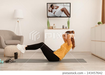 Focused Young Black Woman Engaged In Core Crunch Exercises At Home On Exercise Mat, Displaying Commitment To Fitness And Health. Indoor Setting Promoting Active Lifestyle And Weight Loss Concept. Focused Young Black Woman Engaged In Core Crunch Exercises At Home On Exercise Mat, Displaying Commitment To Fitness And Health. Indoor Setting Promoting Active Lifestyle And Weight Loss Concept. 143457642