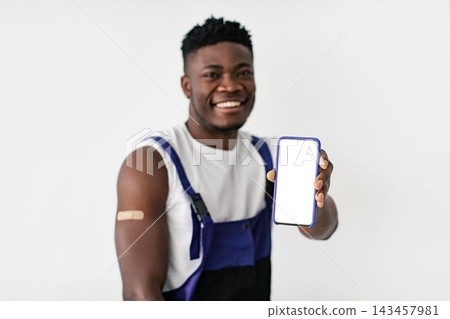 Smiling Young Black Man Showing Smartphone With Blank Screen While Standing In Studio Setting, Presenting Mobile Technology. Cheerful Millennial Male Happy To Share Information Via Device. Smiling Young Black Man Showing Smartphone With Blank Screen While Standing In Studio Setting, Presenting Mobile Technology. Cheerful Millennial Male Happy To Share Information Via Device. 143457981