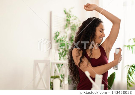 Smiling Hispanic Woman In Her 20s Applying Deodorant In Bathroom, Taking Care Of Personal Hygiene In A Bright And Inviting Setting. Focused On Skincare Routine, Wellness Concept. Smiling Hispanic Woman In Her 20s Applying Deodorant In Bathroom, Taking Care Of Personal Hygiene In A Bright And Inviting Setting. Focused On Skincare Routine, Wellness Concept. 143458038