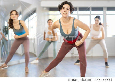 Hispanic woman learning modern street dancing during group class Hispanic woman learning modern street dancing during group class 143458331