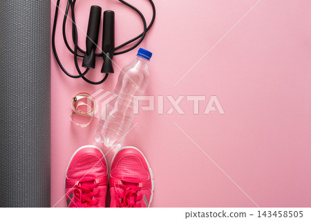Running shoes placed on a pink floor next to a jump rope, a water bottle, and a yoga mat. It indicates preparation for an exercise session or workout routine. Running shoes placed on a pink floor next to a jump rope, a water bottle, and a yoga mat. It indicates preparation for an exercise session or workout routine. 143458505
