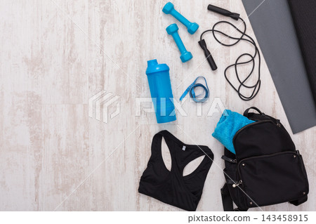 Different items for exercise are set on the floor including dumbbells, a shaker, a mat, and a bag. This setup shows a workout space ready for use at a fitness area. Different items for exercise are set on the floor including dumbbells, a shaker, a mat, and a bag. This setup shows a workout space ready for use at a fitness area. 143458915