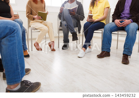 Several people sit in a circle in a well-lit room. They listen to each other and take notes. Some hold notebooks, while others have drinks. The atmosphere is focused on sharing thoughts. Several people sit in a circle in a well-lit room. They listen to each other and take notes. Some hold notebooks, while others have drinks. The atmosphere is focused on sharing thoughts. 143459232