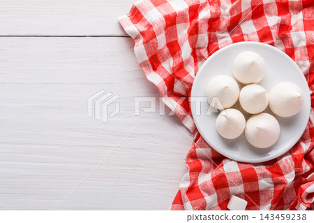 A plate holds six round white treats placed on a red checkered cloth. The background is wooden and adds a simple touch to the scene, which showcases a food arrangement. A plate holds six round white treats placed on a red checkered cloth. The background is wooden and adds a simple touch to the scene, which showcases a food arrangement. 143459238