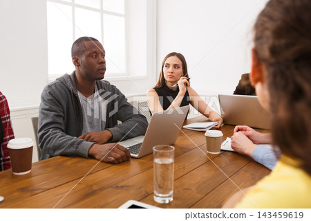 A group of team members engages in a meeting around a wooden table. Participants listen and take notes while using laptops. The atmosphere is focused and collaborative as they discuss important tasks. A group of team members engages in a meeting around a wooden table. Participants listen and take notes while using laptops. The atmosphere is focused and collaborative as they discuss important tasks. 143459619