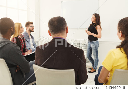 A woman stands in front of a group of people in a classroom. The group appears engaged as they listen to her speak. The setting has bright natural light coming from windows. A woman stands in front of a group of people in a classroom. The group appears engaged as they listen to her speak. The setting has bright natural light coming from windows. 143460046