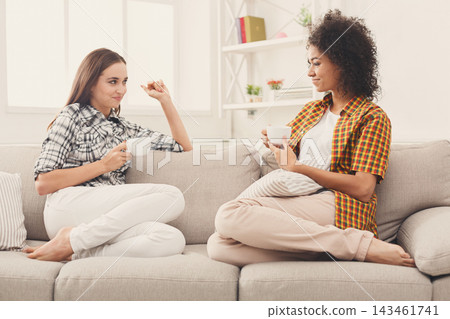 Two friends sit on a couch in a bright room, sharing coffee and conversation. They wear casual clothing and show smiles, creating a relaxed atmosphere in the afternoon sun. Two friends sit on a couch in a bright room, sharing coffee and conversation. They wear casual clothing and show smiles, creating a relaxed atmosphere in the afternoon sun. 143461741