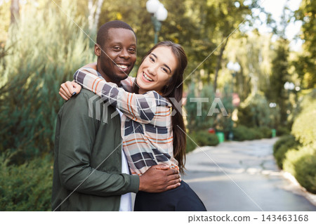 Two people stand together in a park surrounded by greenery. They smile at the camera while hugging. The sun shines on a clear day. The path is lined with trees and bushes. Two people stand together in a park surrounded by greenery. They smile at the camera while hugging. The sun shines on a clear day. The path is lined with trees and bushes. 143463168