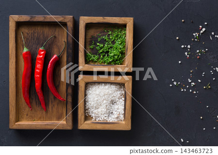 Three wooden trays hold red chilies, herbs, and sea salt arranged on a dark surface. Different textures and colors create a visual contrast, perfect for cooking preparations. Three wooden trays hold red chilies, herbs, and sea salt arranged on a dark surface. Different textures and colors create a visual contrast, perfect for cooking preparations. 143463723