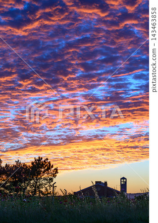A dramatic sunset sky filled with crimson clouds and a field of blooming flowers. A dramatic sunset sky filled with crimson clouds and a field of blooming flowers. 143463858
