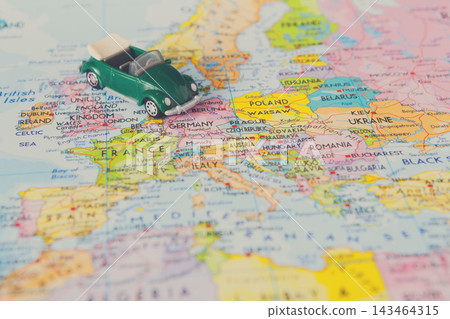 A small green toy car is placed on a map of Europe. The map displays different countries including Germany, Italy, and France. The car highlights travel and exploration in this region. A small green toy car is placed on a map of Europe. The map displays different countries including Germany, Italy, and France. The car highlights travel and exploration in this region. 143464315