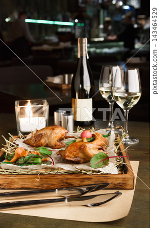A table is set with roasted chicken, salad, and wine. Two glasses of white wine and a candle add to the dinner ambiance. The setting shows a restaurant with a relaxed vibe in the evening. A table is set with roasted chicken, salad, and wine. Two glasses of white wine and a candle add to the dinner ambiance. The setting shows a restaurant with a relaxed vibe in the evening. 143464529