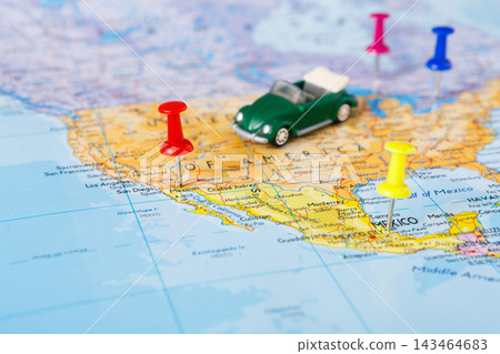 A green toy car sits on a map of the United States. Colorful pushpins mark various locations. The scene shows interest in travel and exploration of different places. A green toy car sits on a map of the United States. Colorful pushpins mark various locations. The scene shows interest in travel and exploration of different places. 143464683
