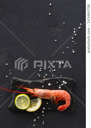 Fresh shrimp is placed on a black stone plate alongside slices of lemon. White salt is scattered around the dish. This setup is in a kitchen with a simple and clean style. Fresh shrimp is placed on a black stone plate alongside slices of lemon. White salt is scattered around the dish. This setup is in a kitchen with a simple and clean style. 143464706