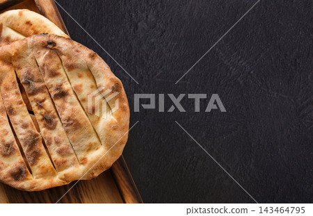 Flatbread sits on a wooden tray. It shows grill marks and has a warm, inviting look. This setting suggests a dining experience where bread is served fresh. Flatbread sits on a wooden tray. It shows grill marks and has a warm, inviting look. This setting suggests a dining experience where bread is served fresh. 143464795