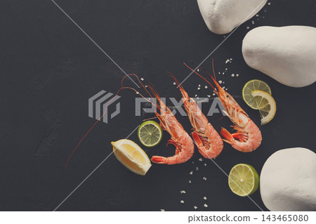 Fresh shrimp are arranged on a dark surface with slices of lemon and lime. White stones are placed nearby, creating a simple setup that highlights the seafood. Fresh shrimp are arranged on a dark surface with slices of lemon and lime. White stones are placed nearby, creating a simple setup that highlights the seafood. 143465080