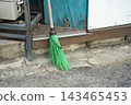 Green Plastic Cleaning Broom Leaning against Old Wooden Storefront Entrance Wall 143465453