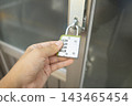 Person Hand Holding and Unlocking Combination Padlock on Glass Door Handle 143465454