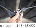 Close Up of Hand Turning Number Dial on Black Wire Cable Lock for Security 143465455