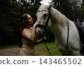 Woman in lace lingerie stroking a white horse in a clearing 143465502