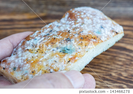A hand holding a slice of moldy bread over a wooden background A hand holding a slice of moldy bread over a wooden background 143466278