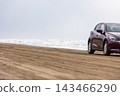 A passenger car driving on the sandy beach and the rough sea. 143466290