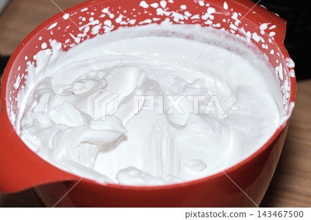 Close-up of freshly whipped cream inside a red plastic mixing bowl on a table Close-up of freshly whipped cream inside a red plastic mixing bowl on a table 143467500
