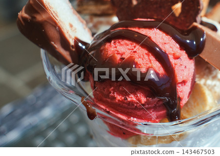 Close-up of delicious raspberry ice cream dessert served in a glass bowl with chocolate syrup Close-up of delicious raspberry ice cream dessert served in a glass bowl with chocolate syrup 143467503
