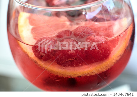 Close-up view of a refreshing pink gin cocktail garnished with fresh raspberries and citrus slices 143467641