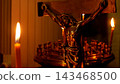 Cross and Crucifix of Jesus Christ with a Burning Candle in a Church 143468500
