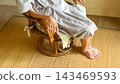 An elderly woman sitting on a wisteria chair, diagonally in front. 143469593