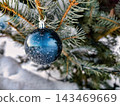 A Christmas tree stands in the snow, adorned with shiny ornaments. The scene captures the festive spirit during the holiday season 143469669