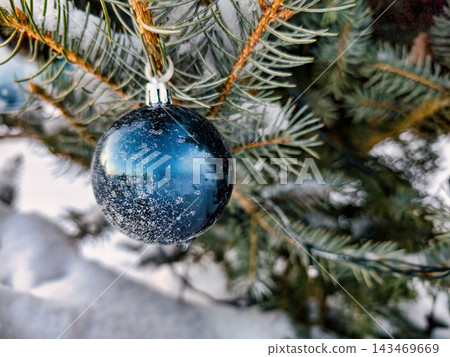 A Christmas tree stands in the snow, adorned with shiny ornaments. The scene captures the festive spirit during the holiday season A Christmas tree stands in the snow, adorned with shiny ornaments. The scene captures the festive spirit during the holiday season 143469669