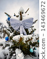 A Christmas and New Year tree stands in the snow. The tree features decorations and a large fabric bow. It is winter with snow covering the branches 143469672