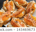 Small pieces of bread are topped with soft cheese, thin salmon slices, and bright orange pieces. This dish is set on a white plate 143469673