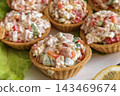 Crispy tart shells hold a filling made of diced vegetables and meat. The dish is arranged on a green leaf with a wedge of lemon beside it 143469674