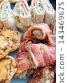 A variety of food is laid out on a blue plate. It includes wraps with vegetables, meat rolls wrapped in bacon, and small savory pastries, likely shared at a gathering 143469675