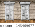 Two white windows on a wooden house show signs of age. The walls are made of light wood, and the windows have peeling paint and broken frames 143469677