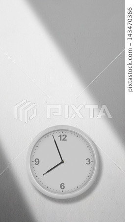 Minimalist white wall clock mounted on a white wall with diagonal sunlight shadows, showing the time. Quotes background Minimalist white wall clock mounted on a white wall with diagonal sunlight shadows, showing the time. Quotes background 143470366