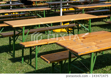 Empty wooden picnic tables arranged on grass in an outdoor venue 143471475