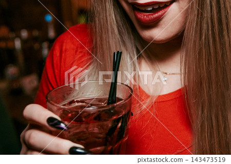 Young woman holding glass cup with alcoholic cocktail in hand in nightclub bar Young woman holding glass cup with alcoholic cocktail in hand in nightclub bar 143473519