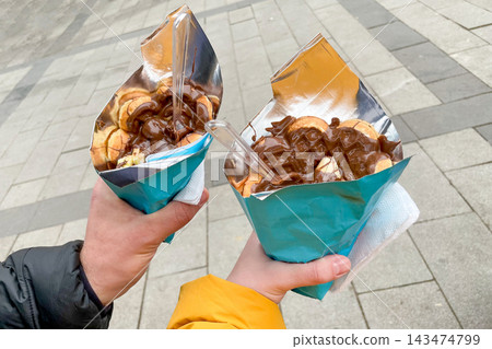 Bubble belgian waffle with chocolate paste in cone, couple hold dessert in hands 143474799